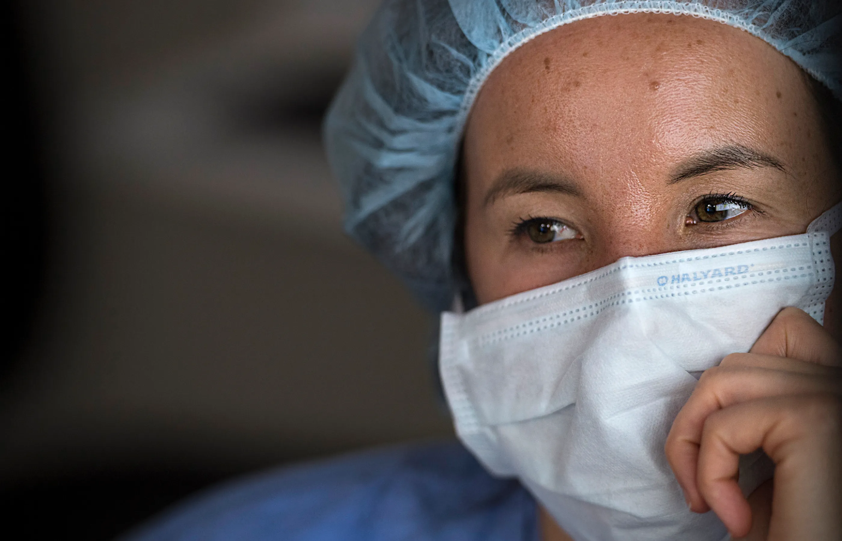 A team member in surgical protective gear (mask and surgical cap) with her hand by her face