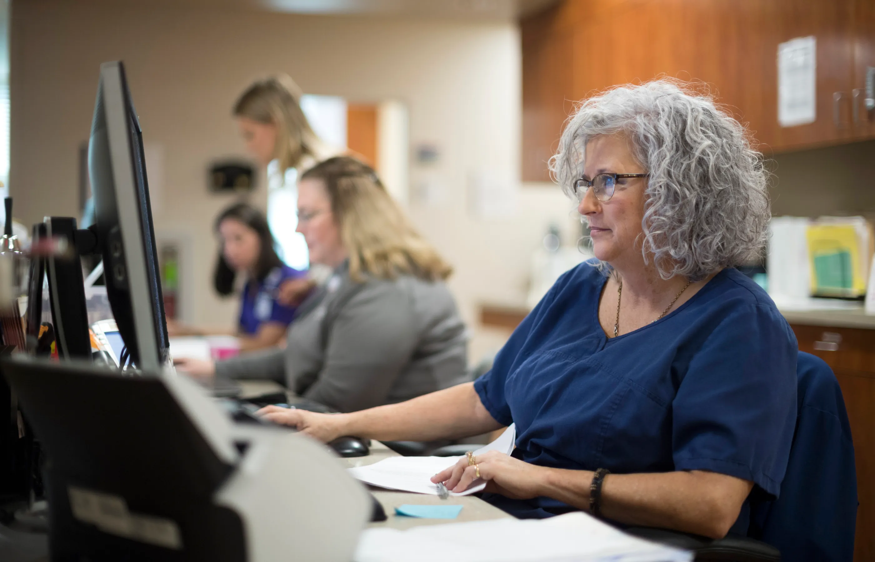 Woman team members in a clinic office reviewing patient information on computer screens