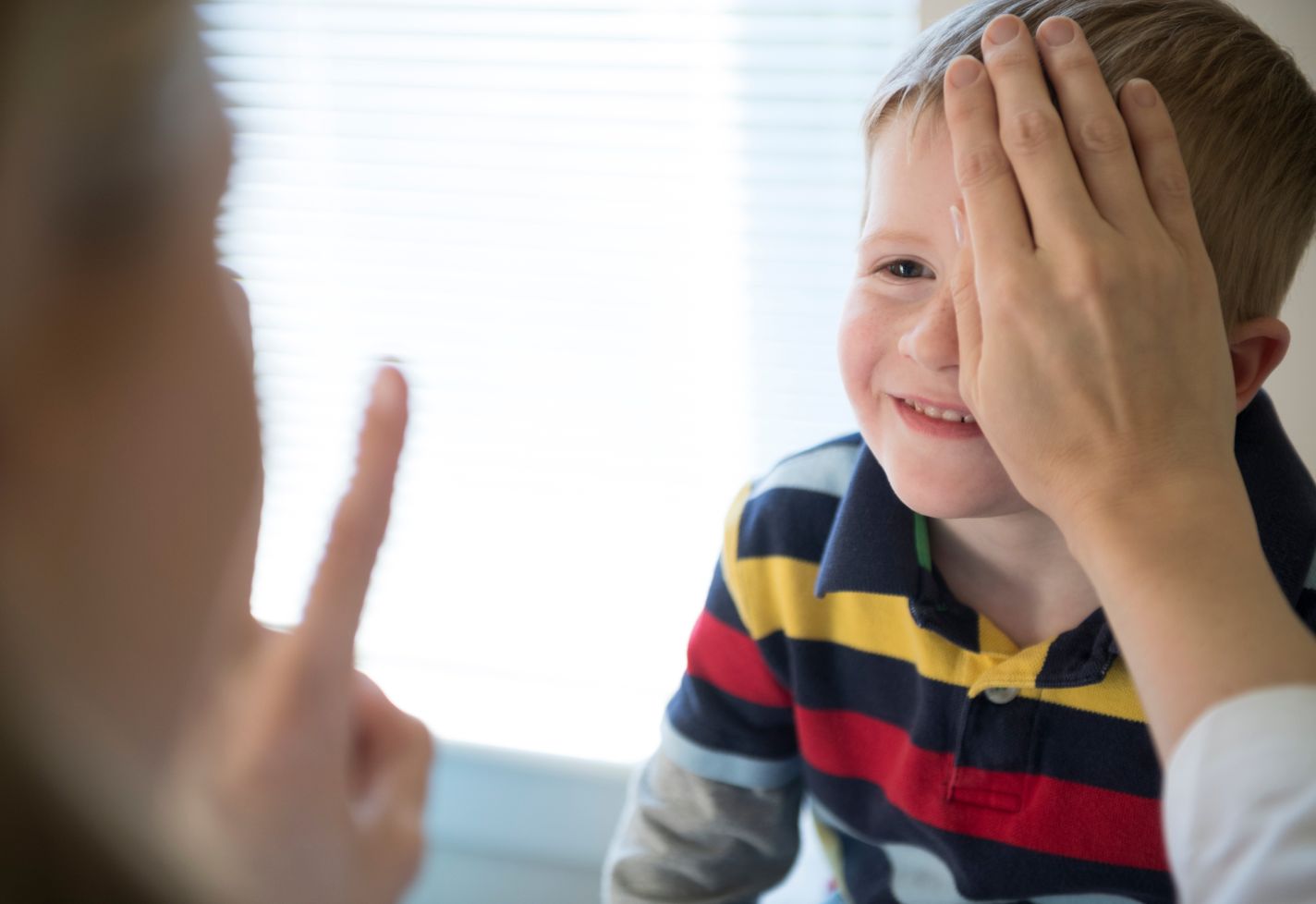 A boy receives an eye exam while a doctor covers one of the boy's eyes.