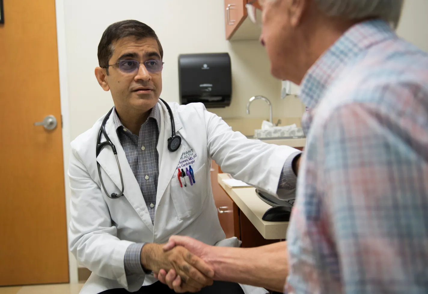 Dr. Tejwani is sitting across from a senior male patient in exam room. The two are shaking hands. 