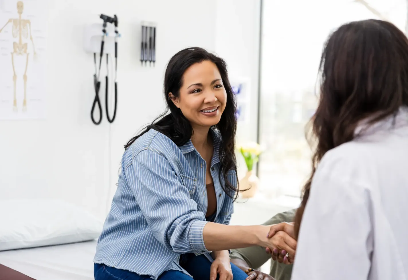 A female patient shaking a female provider's hand in an office.