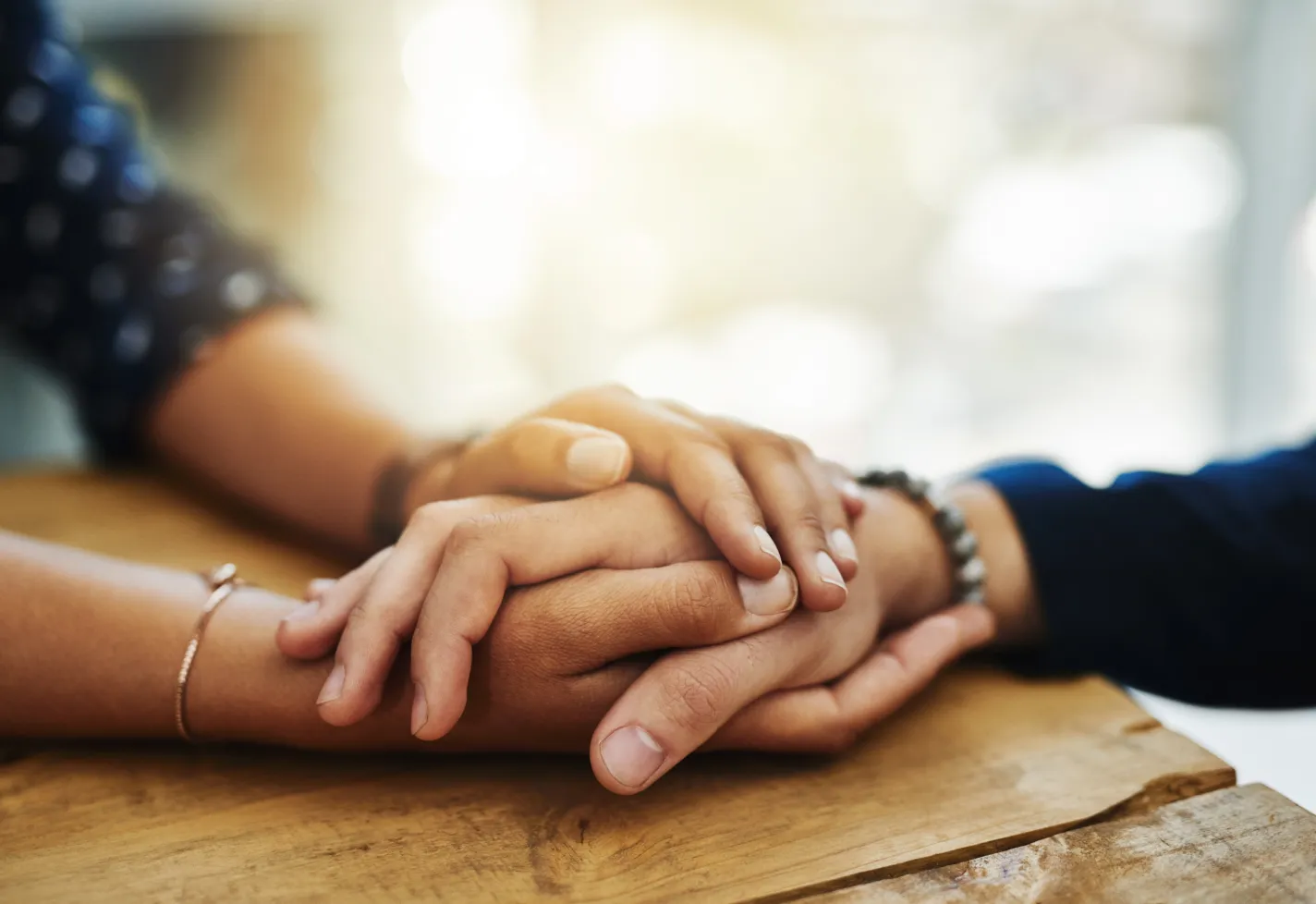Hands holding another person's hand on a wooden table.
