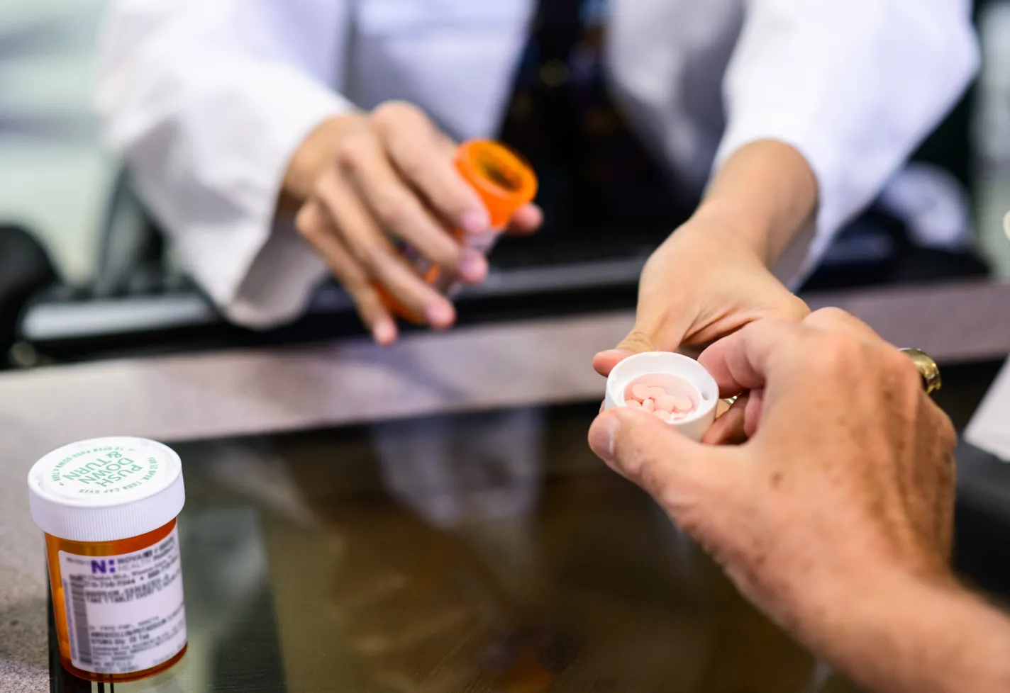 A Novant Health pharmacist has poured some pills into the cap of a pill bottle for the patient. 
