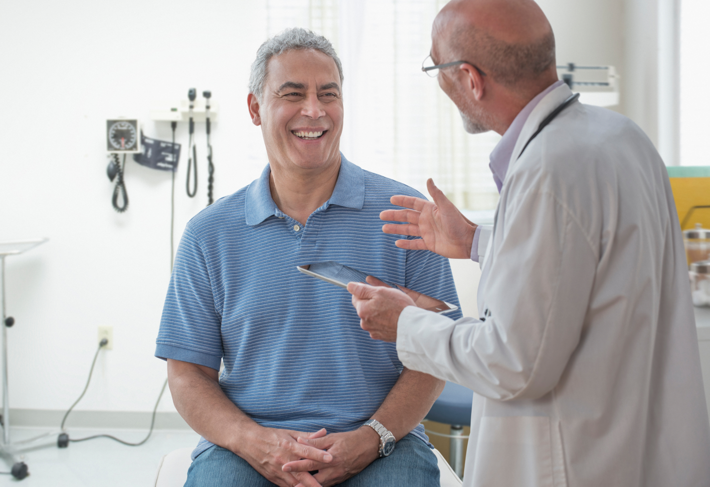 A man in an exam room smiling while speaking with a doctor.