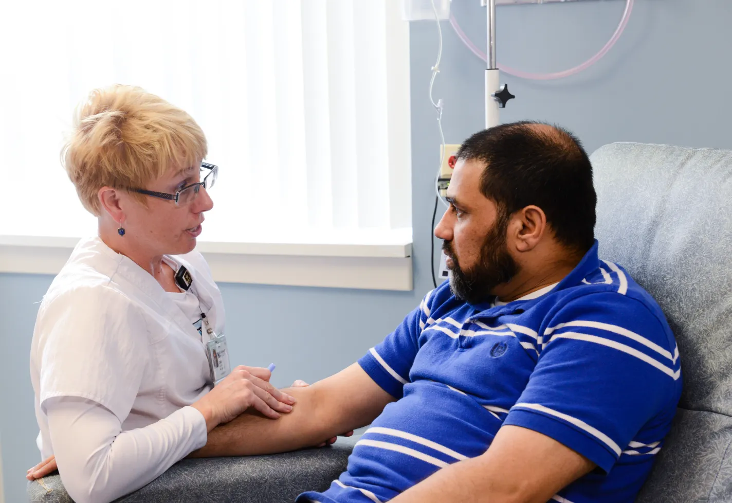 A nurse is kneeling as she talks with a male patient. 