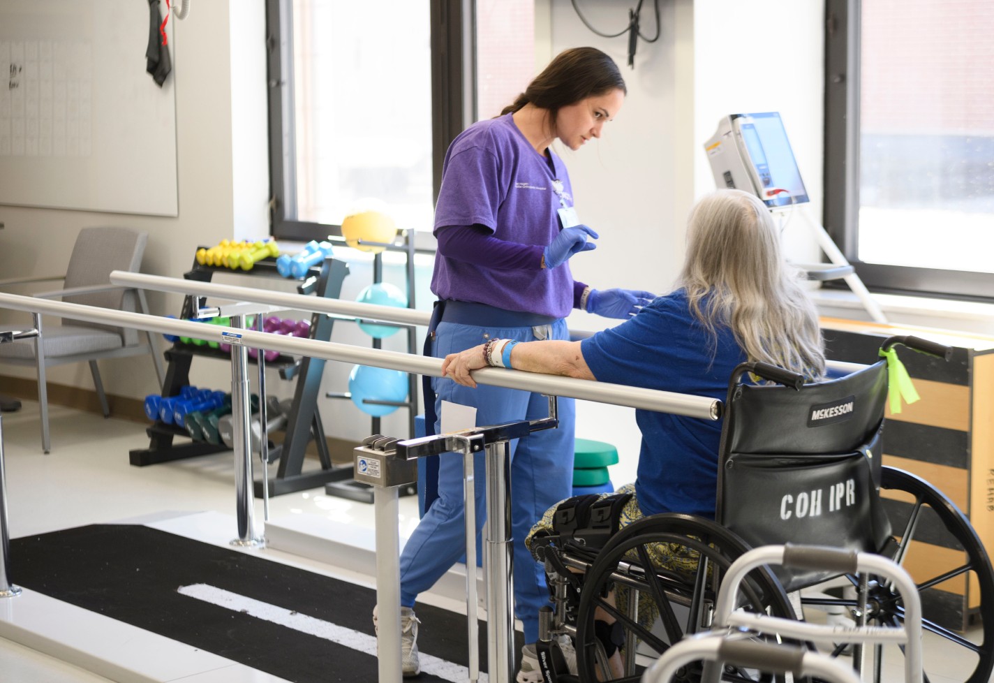 Therapy team member assisting a patient with gait training between parallel bars.