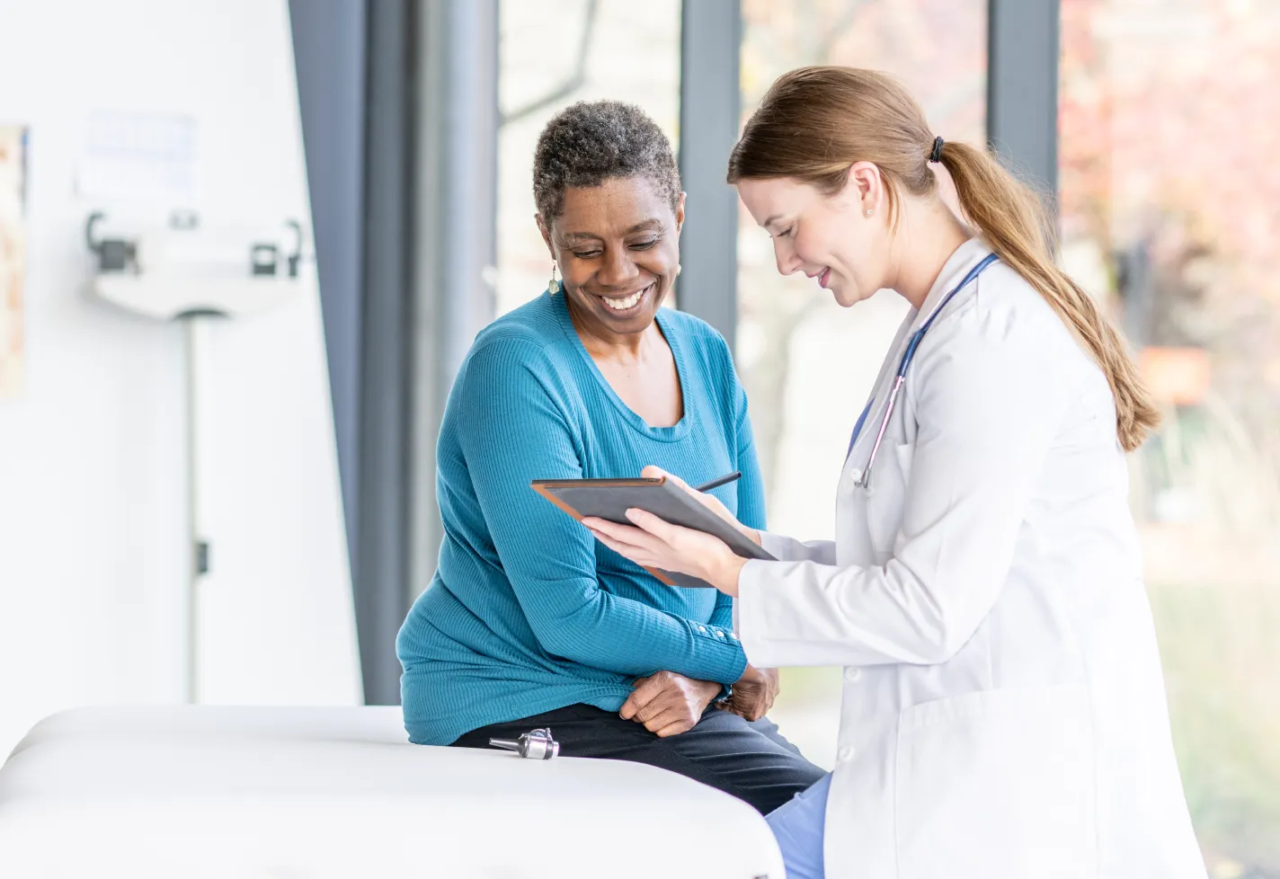 A woman smiles while speaking with a doctor in an exam room.