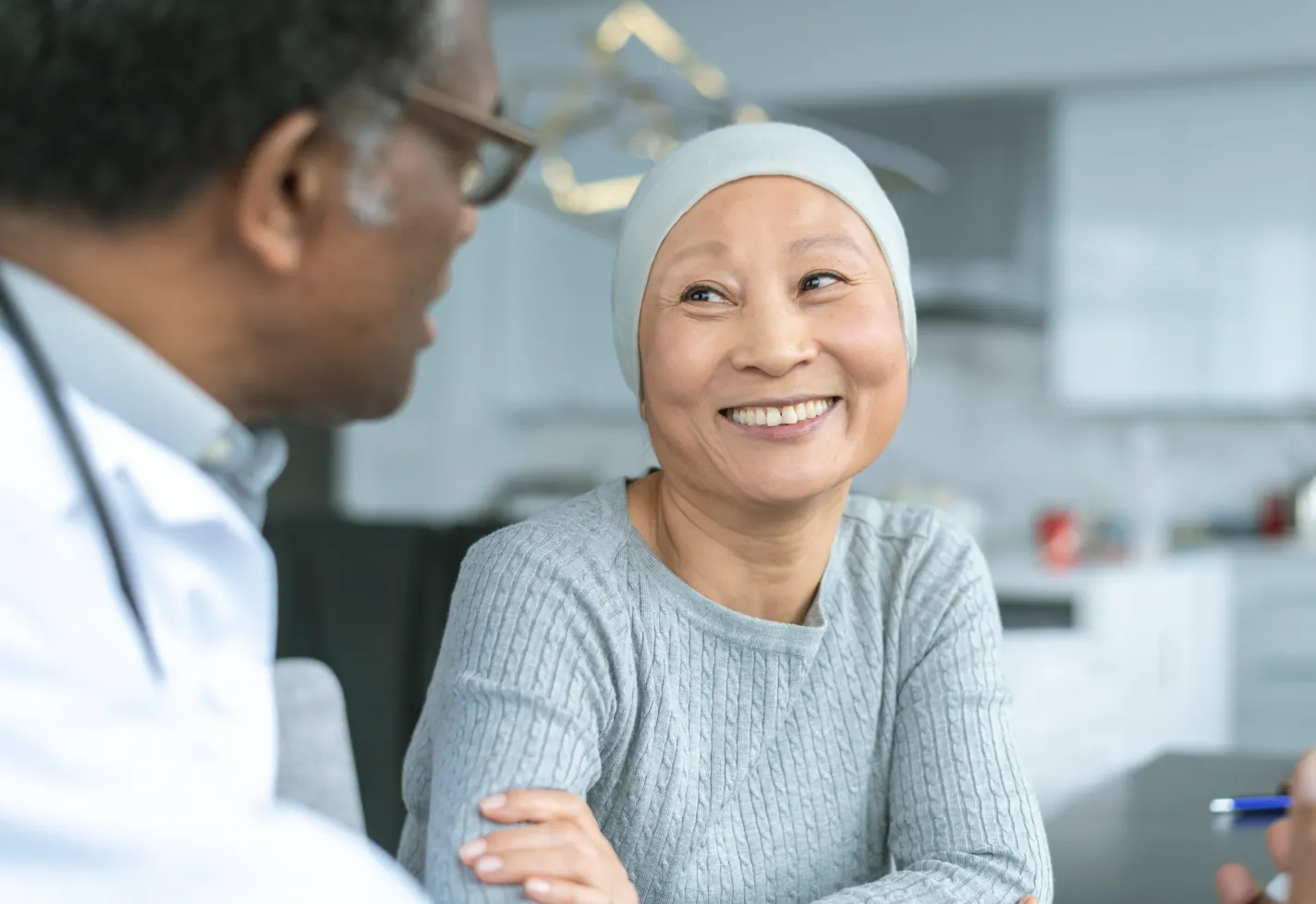A cancer patient is sitting, smiling, and talking with her healthcare provider. 