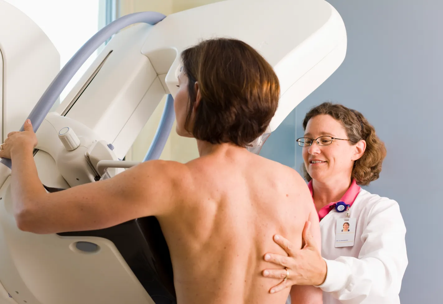 A health care provider is assisting and positioning a woman for a mammogram scan. 