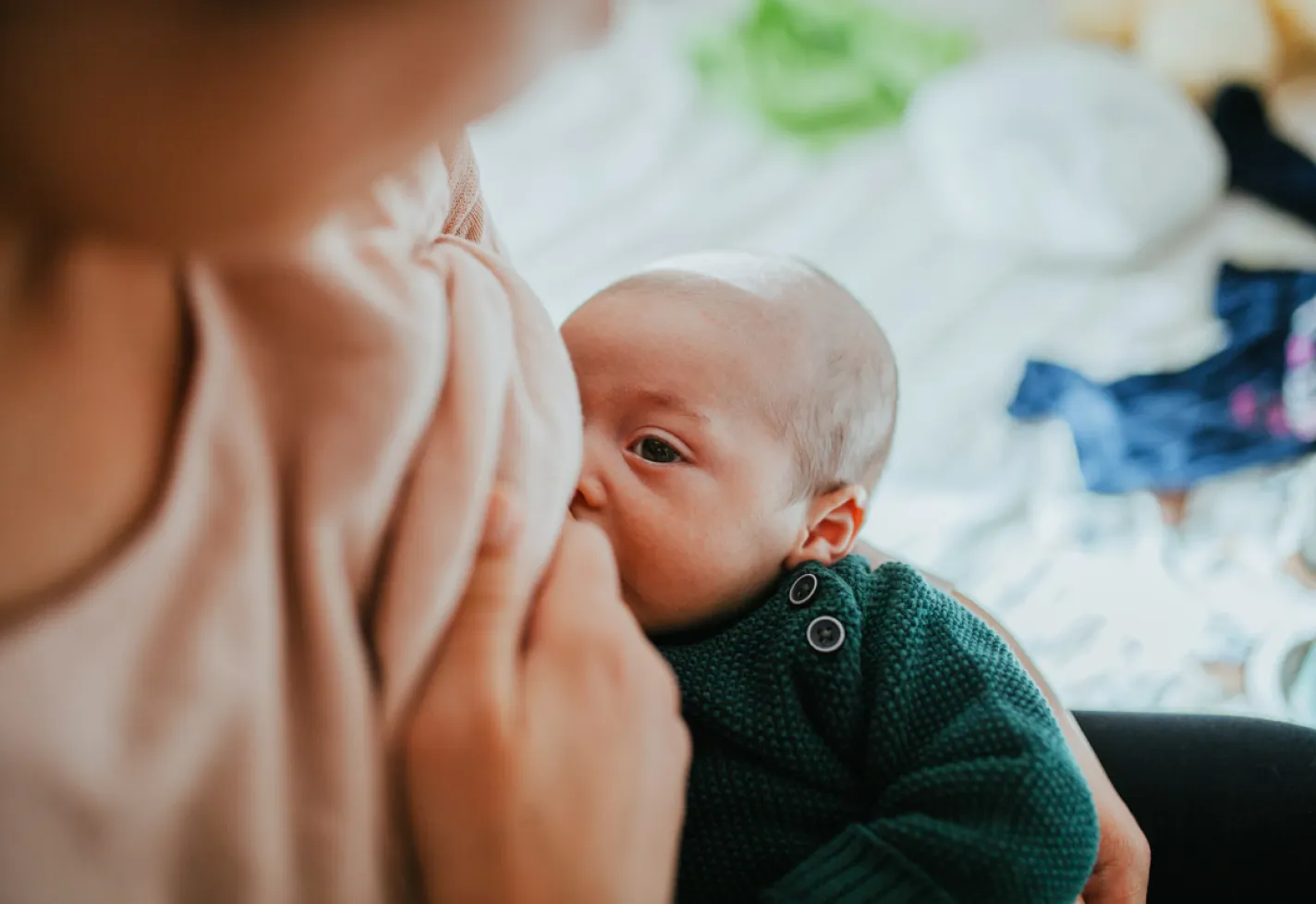 Newborn baby is being held and looking at his mother as she breastfeeds him. 