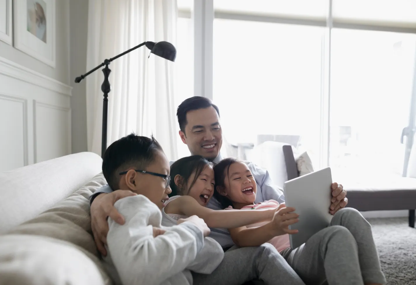 A father is sitting on a couch with his children on a video call. 