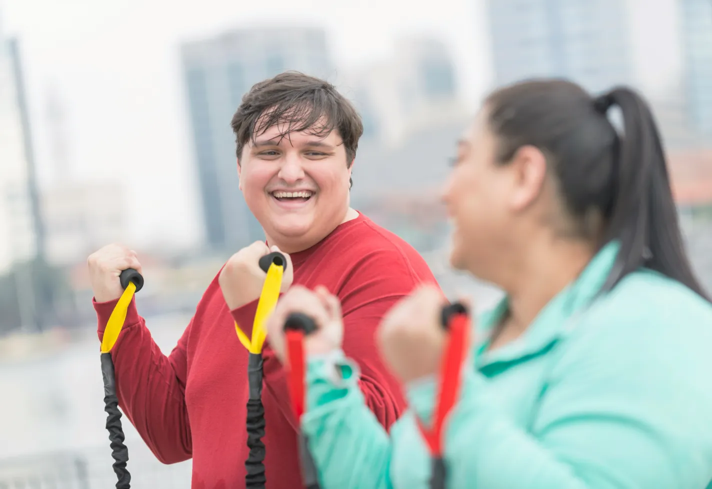 Two friends are smiling at one another as they work out with exercise bands. 