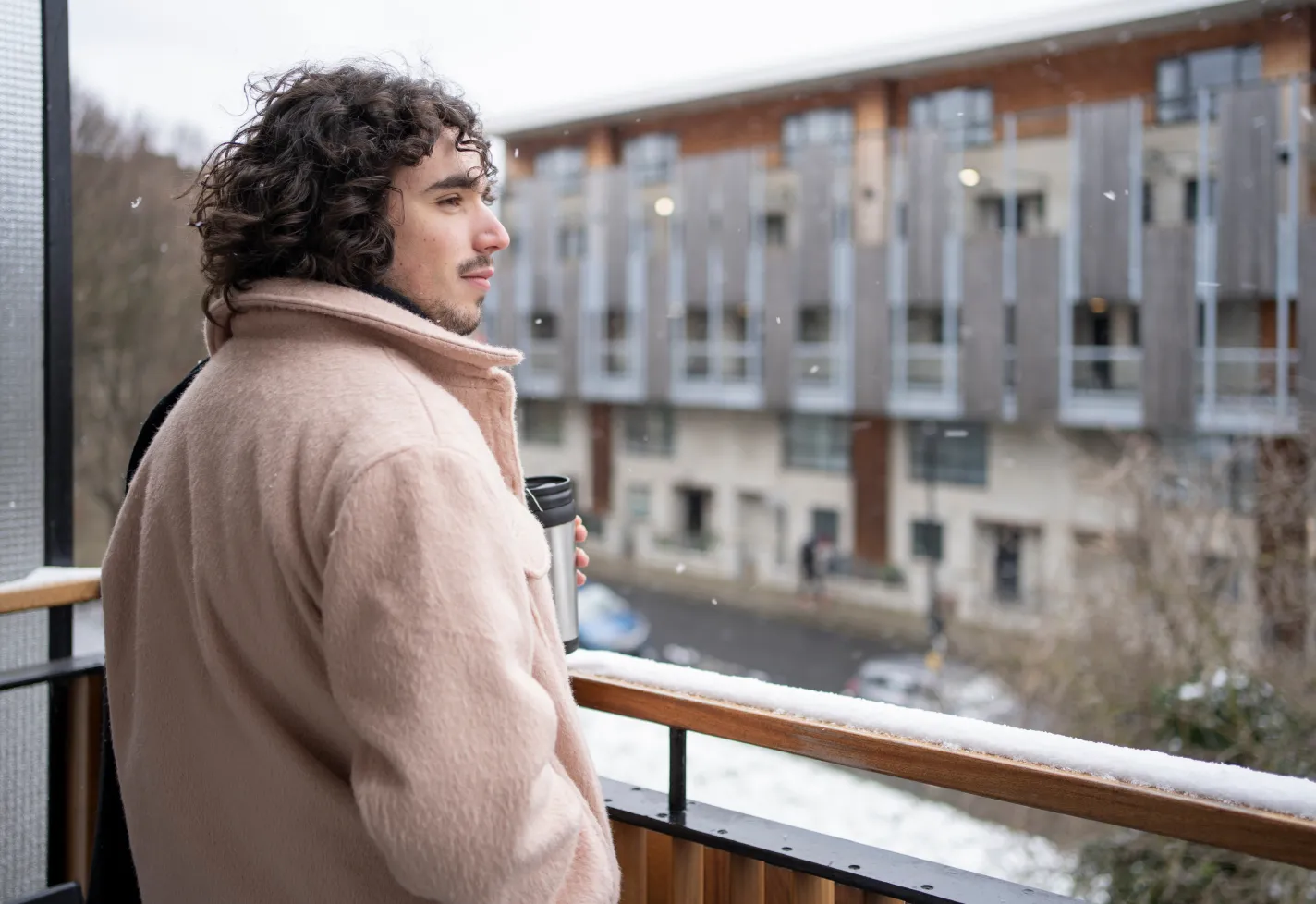 Man with coffee out on a balcony when it is snowing