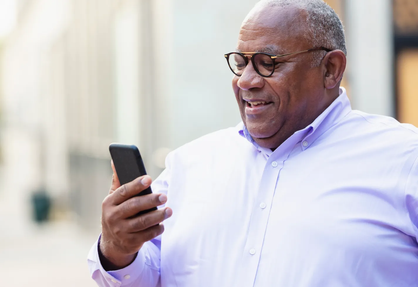 A mature man is standing, smiling, and reviewing information on his smartphone.