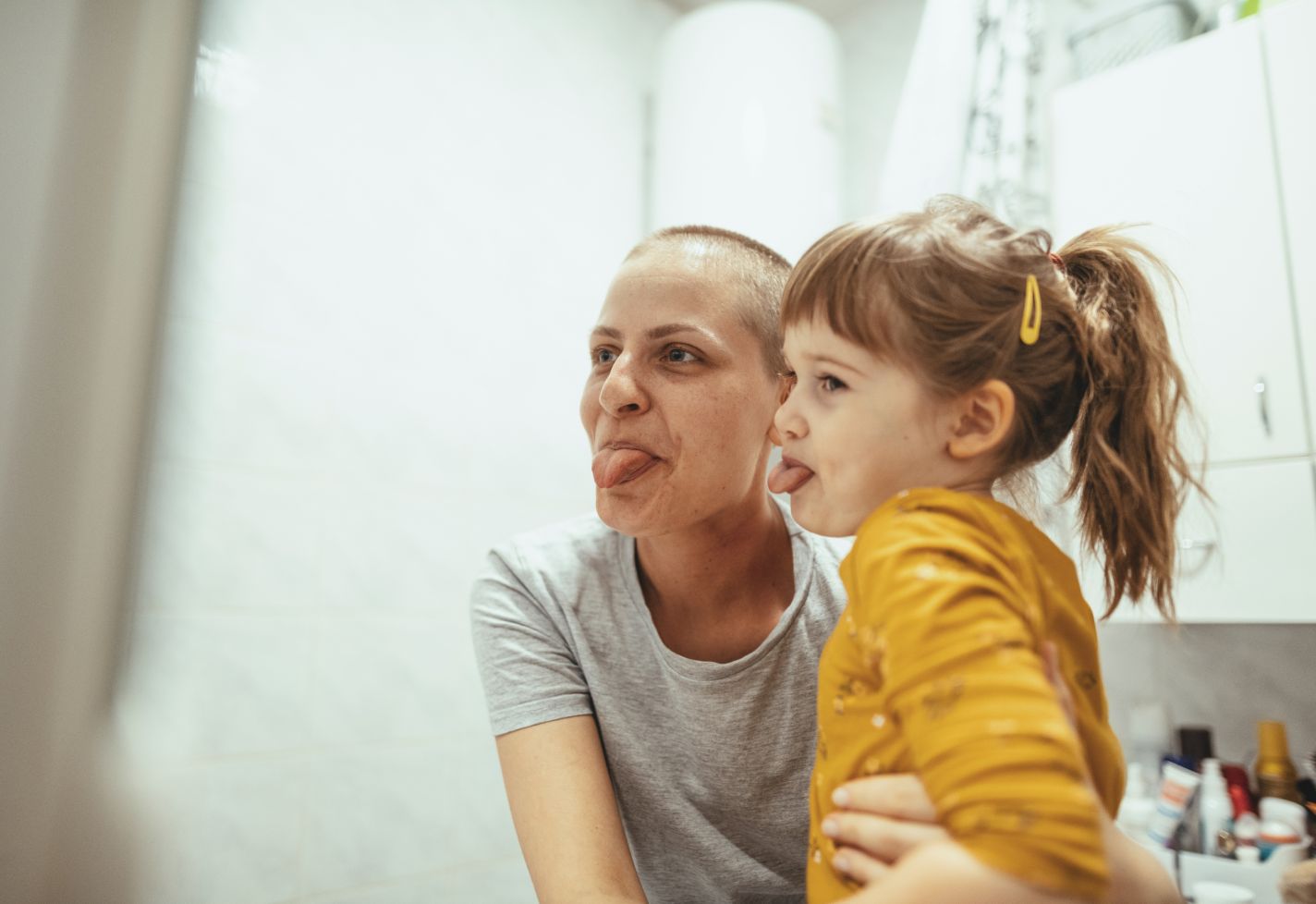 A mother and her daughter making faces in a bathroom mirror.