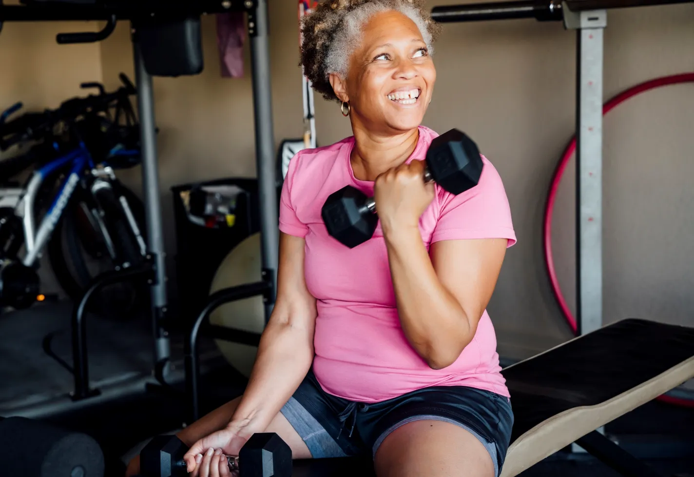 Senior woman working out with dumbbells while sitting on a bench at the gym. 