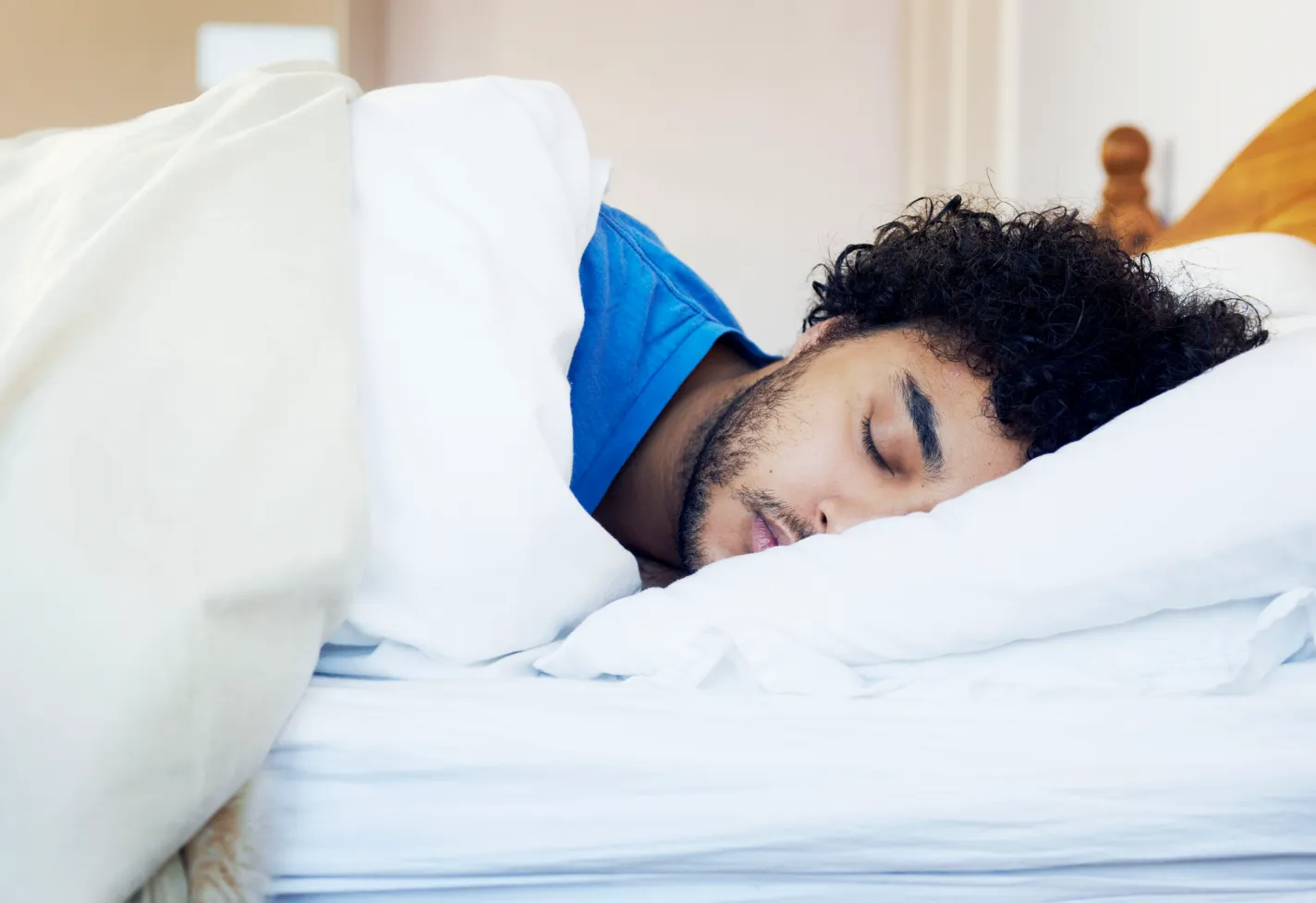 A man with curly hair sleeps in his bed.