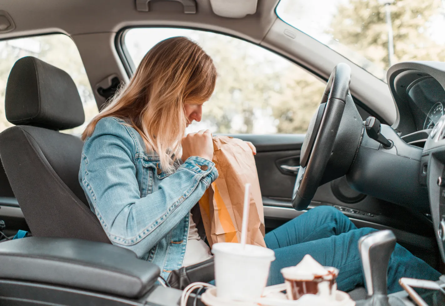 Women sitting in her car looking inside a brown paper bag carrying fast food. 