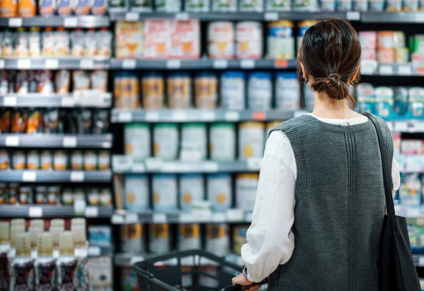 A woman is standing in a grocery store aisle reviewing all of the options. 