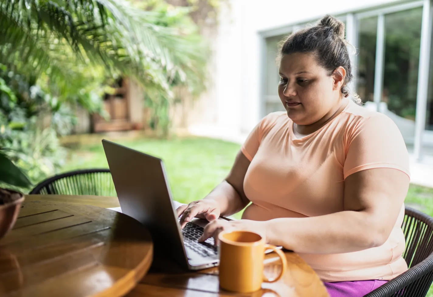 Woman is sitting at a table in her backyard as she types on a laptop. 