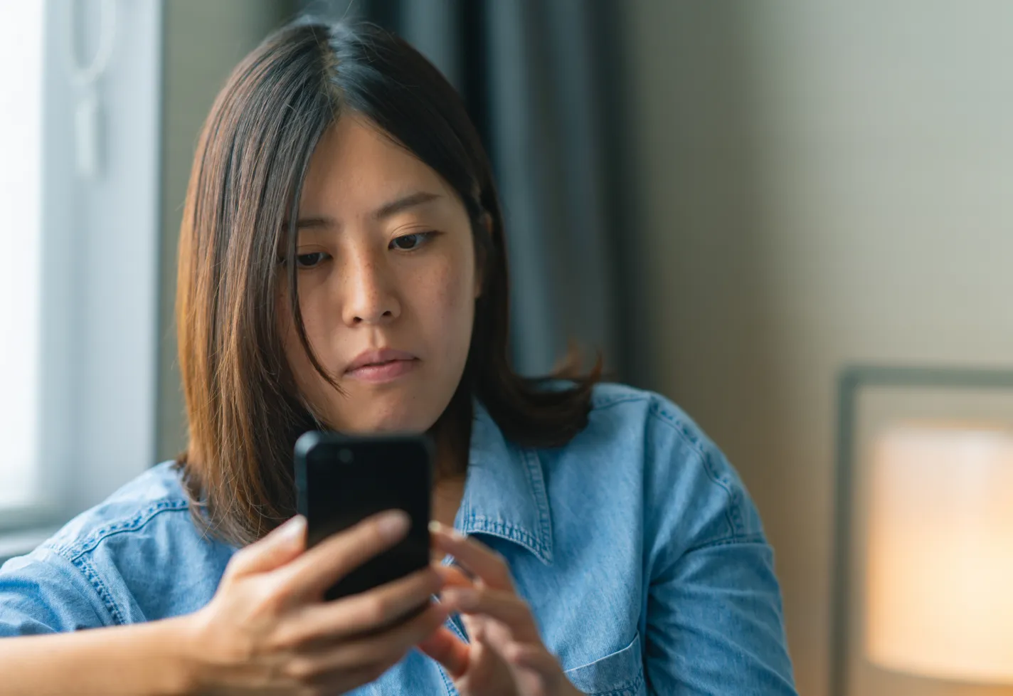 A woman is sitting on a couch viewing information on her phone. 