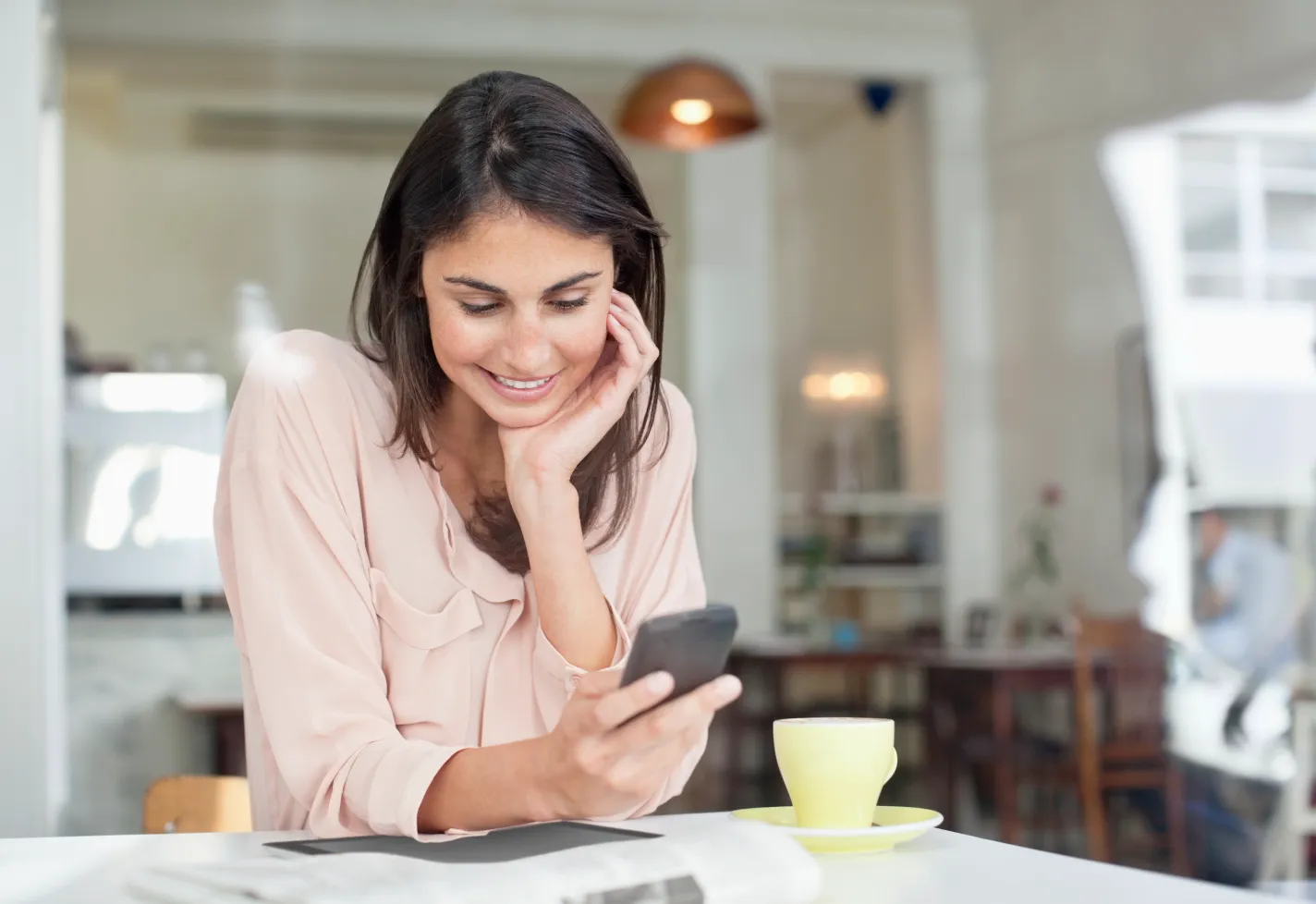 A woman is sitting at a kitchen table viewing information on her phone. 