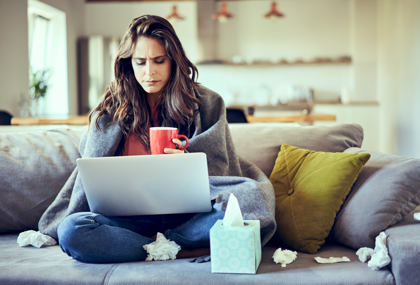 Sick woman sitting on a couch browsing on her laptop