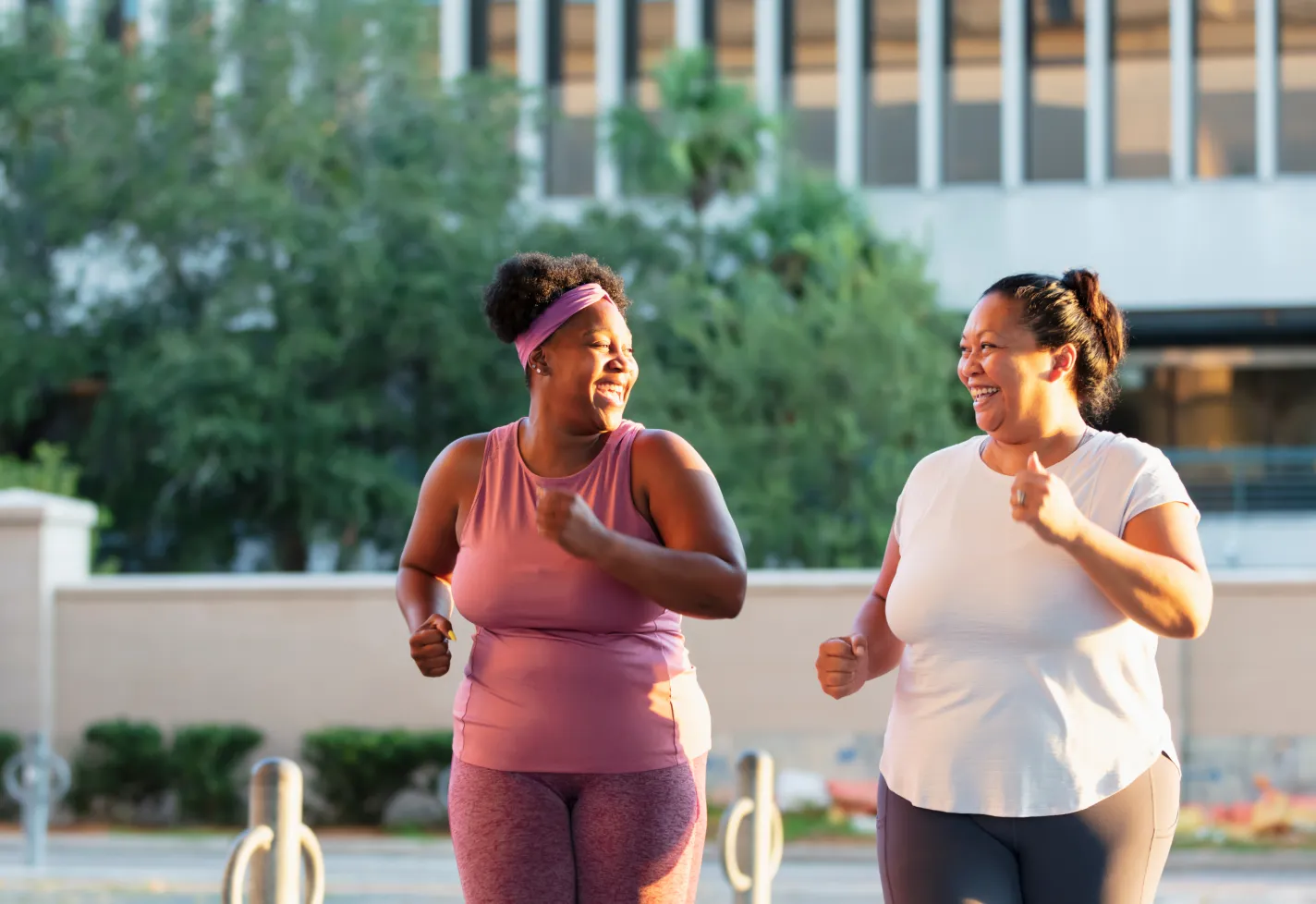 Two women smiling as they jog outdoors in a city.