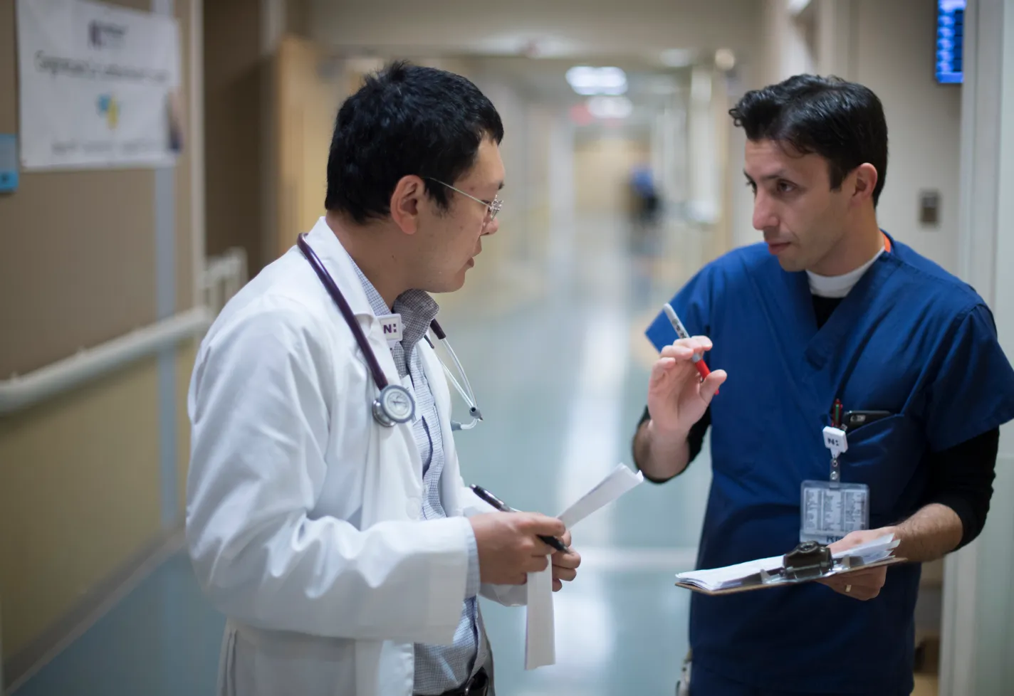 A Novant Health doctor and nurse are standing in the hall of a hospital as they discuss and plan together. 