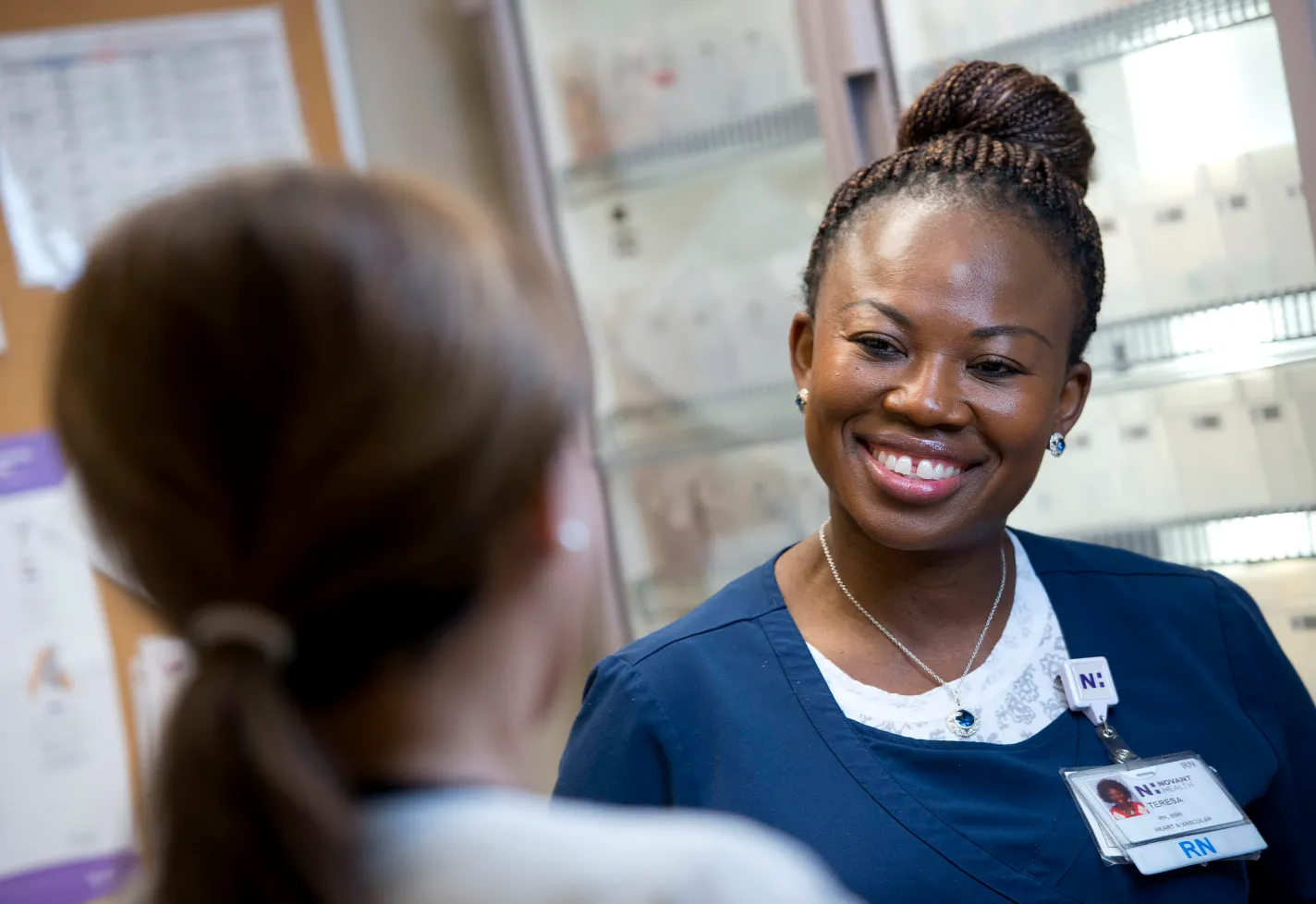 A Novant Health registered nurse is smiling and talking with another team member. 