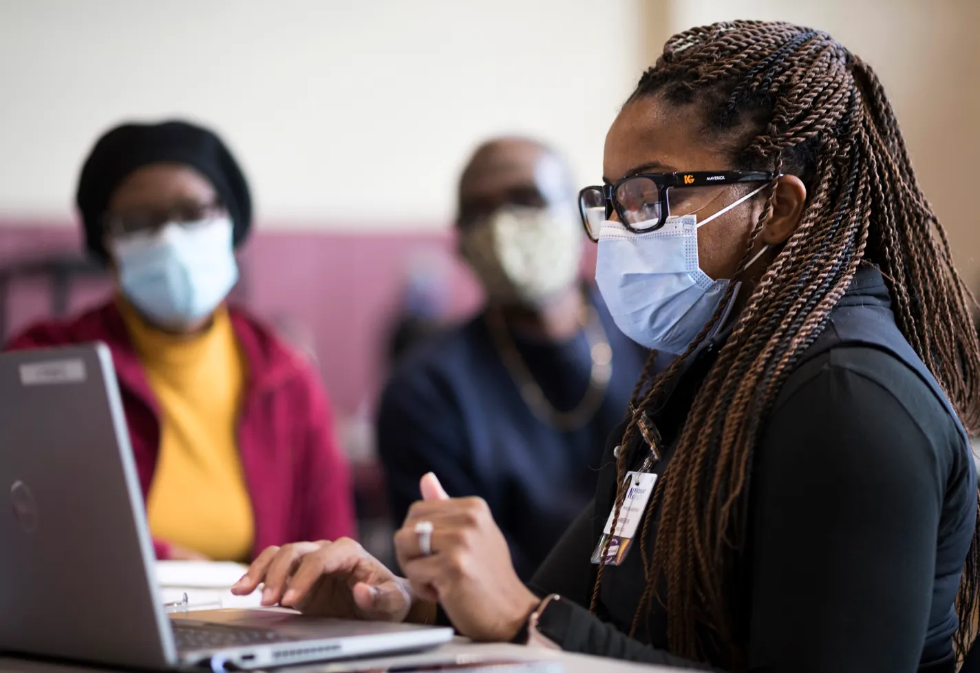 Novant Health team member and couple at a community care event. Everyone is masked and the team member is gathering information on a laptop.