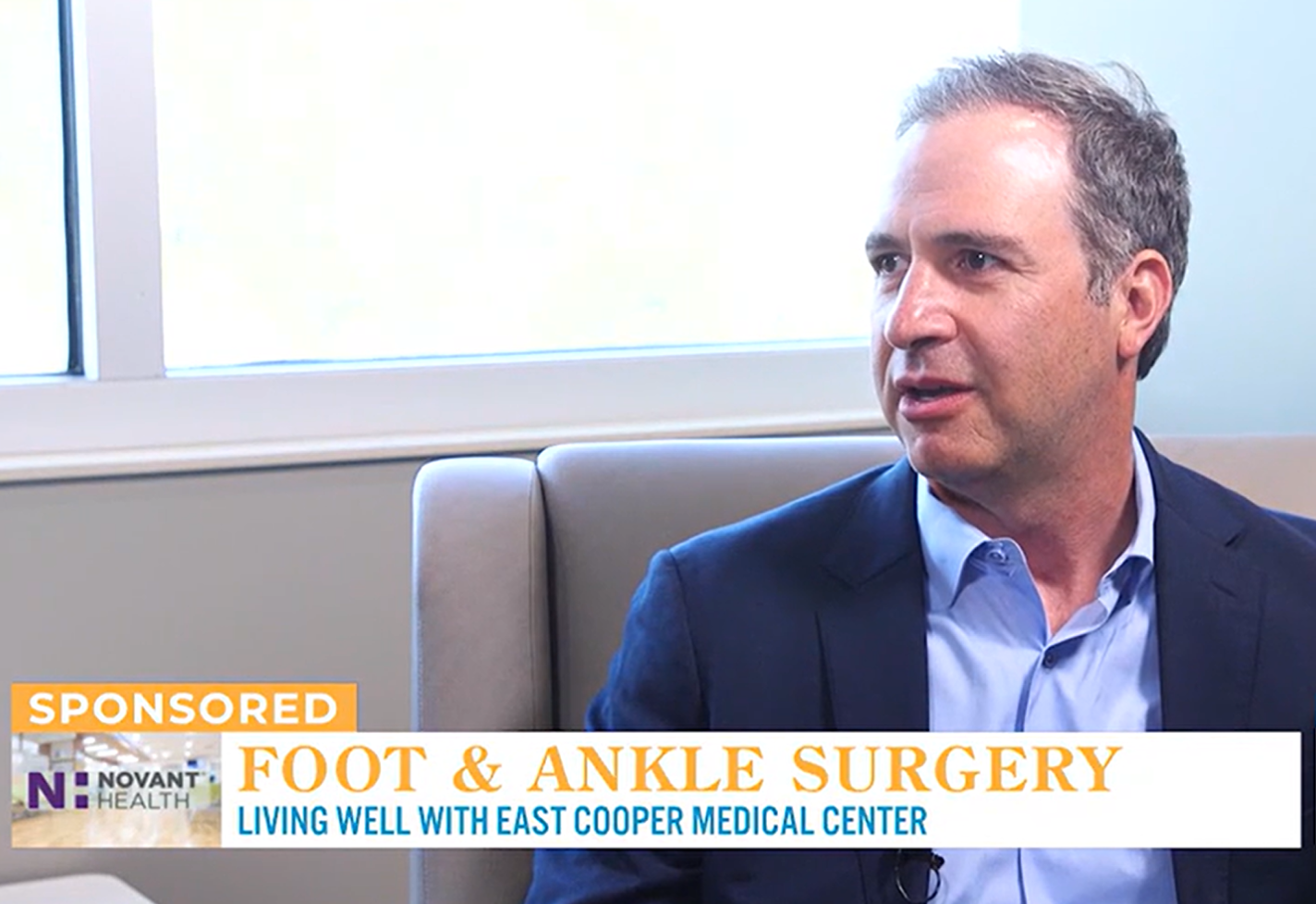 Dr. William Corey in a suit talking about foot and ankle surgery during a health news segment.