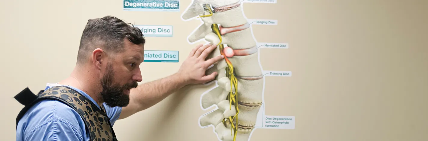 Team member with hand on a wall display of degenerative, bulging, and herniated discs speaking to someone