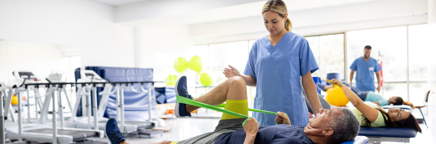 A female physical therapist helping a man exercise his leg in a rehabilitation center.