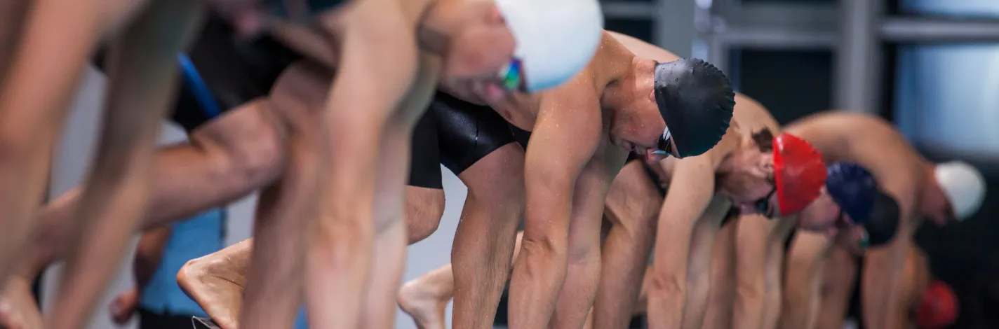 Competitive male swimmers crouching on swimming starting block.