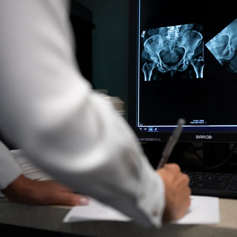 A healthcare provider is writing as they review an x-ray of a patients hip.
