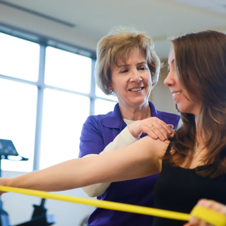 A physical therapist is guiding a woman as she completes exercises. 