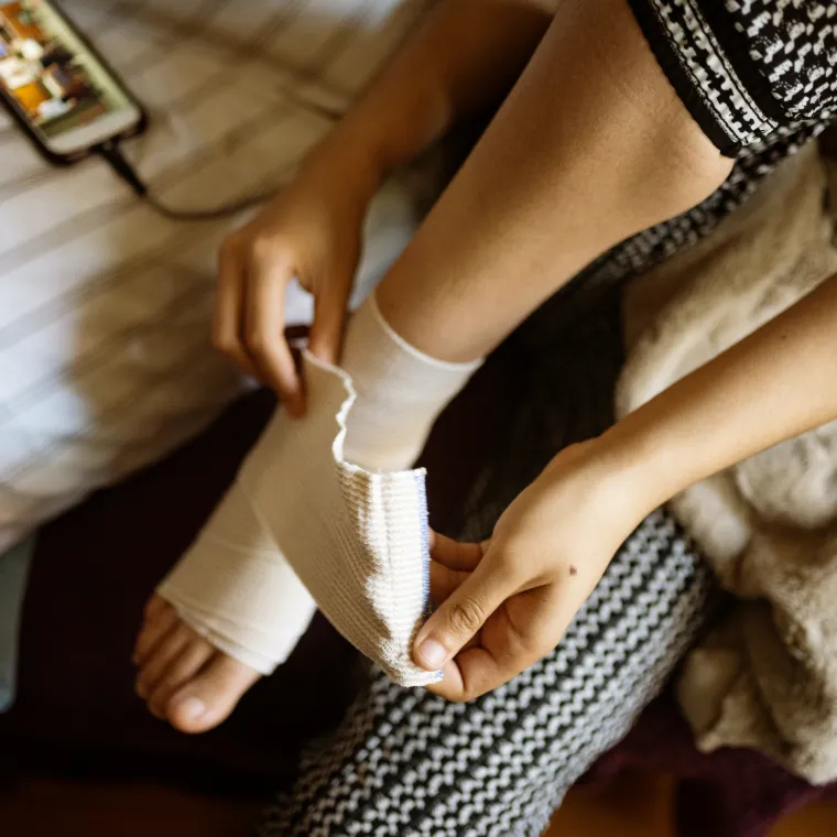 Woman wrapping her sprained ankle at home.