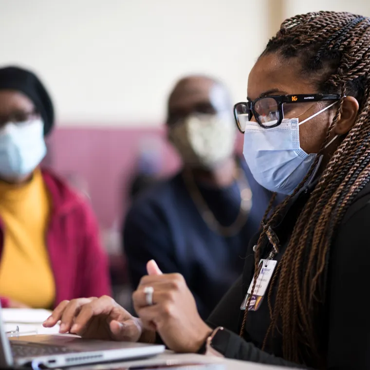 Novant Health team member and couple at a community care event. Everyone is masked and the team member is gathering information on a laptop.