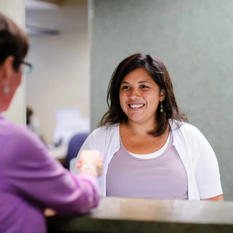 A Novant Health team member is smiling at a patient at the front desk of a clinic. 