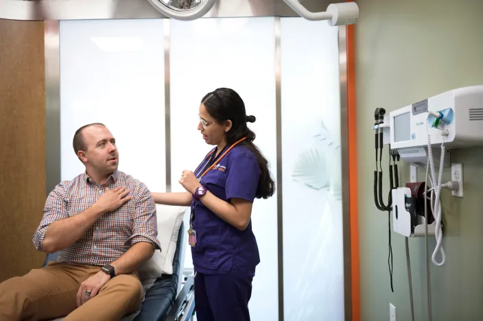 A male patient is talking with a Novant Health nurse in a clinic exam room. 