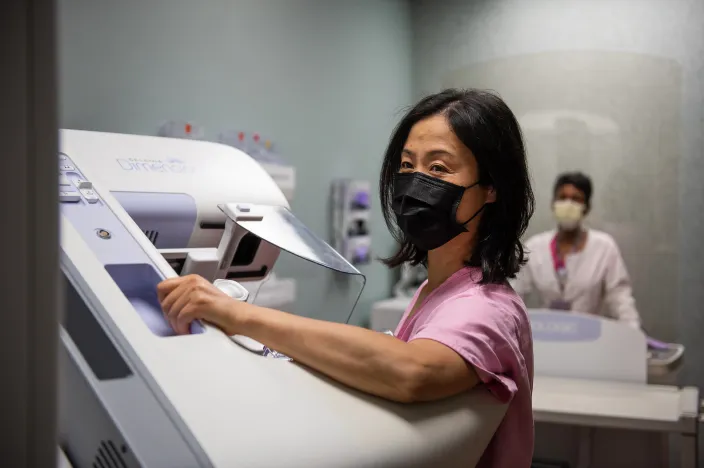 A woman is wearing a mask and pink gown as she is having a mammogram. 