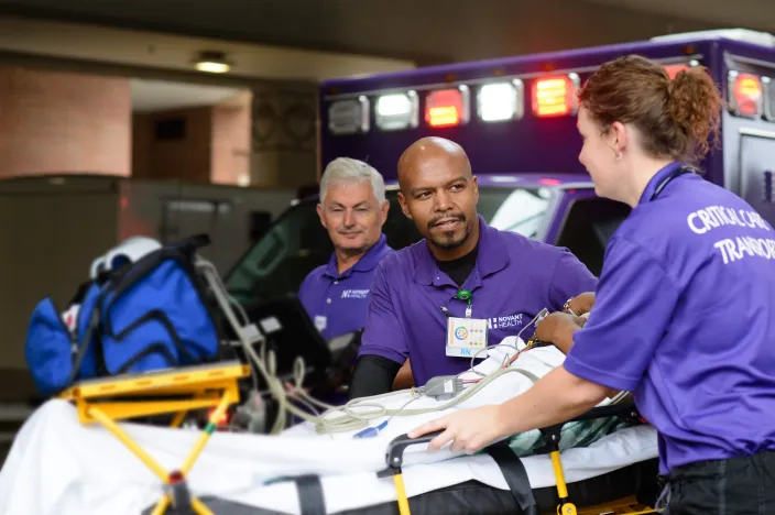 Three Novant Health team members are rolling a patient into a facility on a stretcher. 