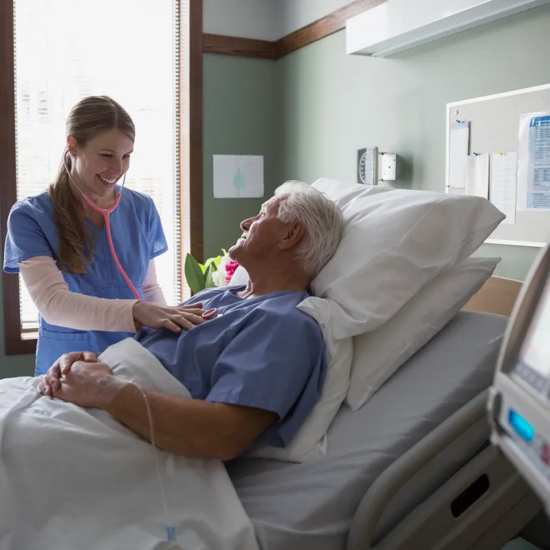 A nurse is listening to a patient's heartbeat as they lay in a hospital bed. 