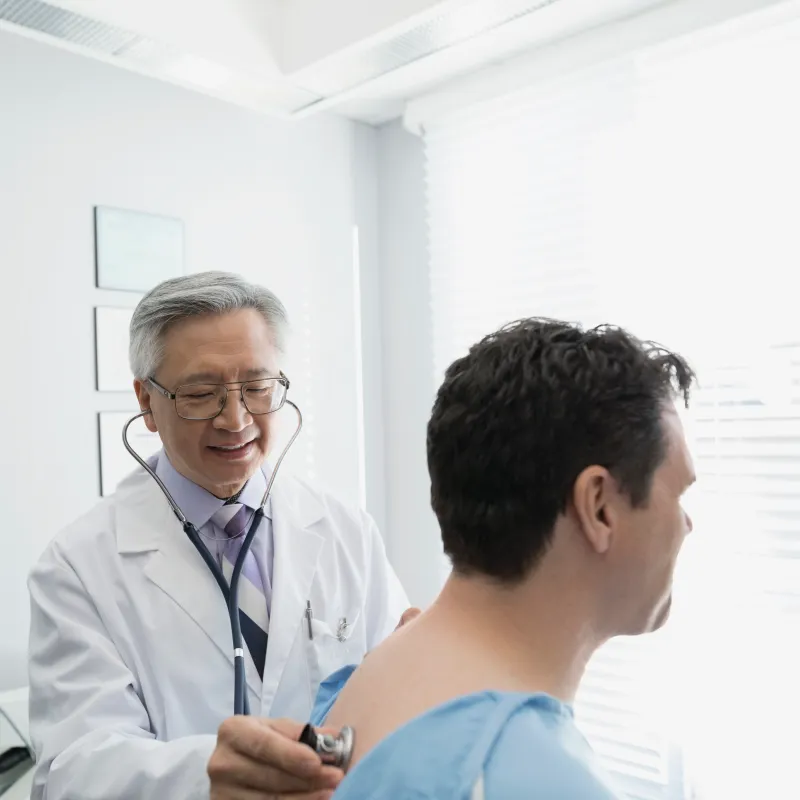 A health care provider has placed a stethoscope on a patient back to listen to their heartbeat. 