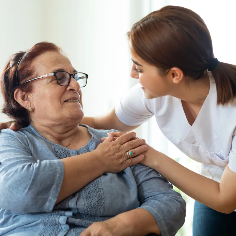 A nurse is leaning over talking with a senior woman patient. 