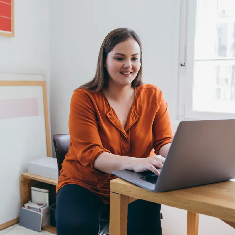 A young woman is sitting at a desk typing on her laptop. 