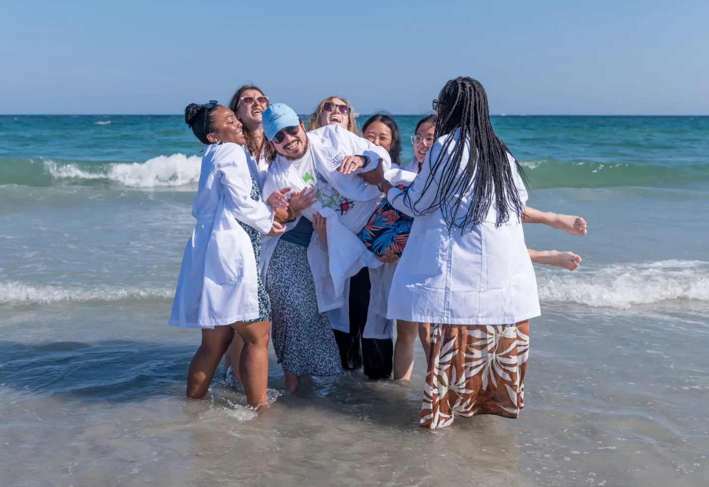Group of Wilmington family medicine residents on the beach shore lifting up one resident