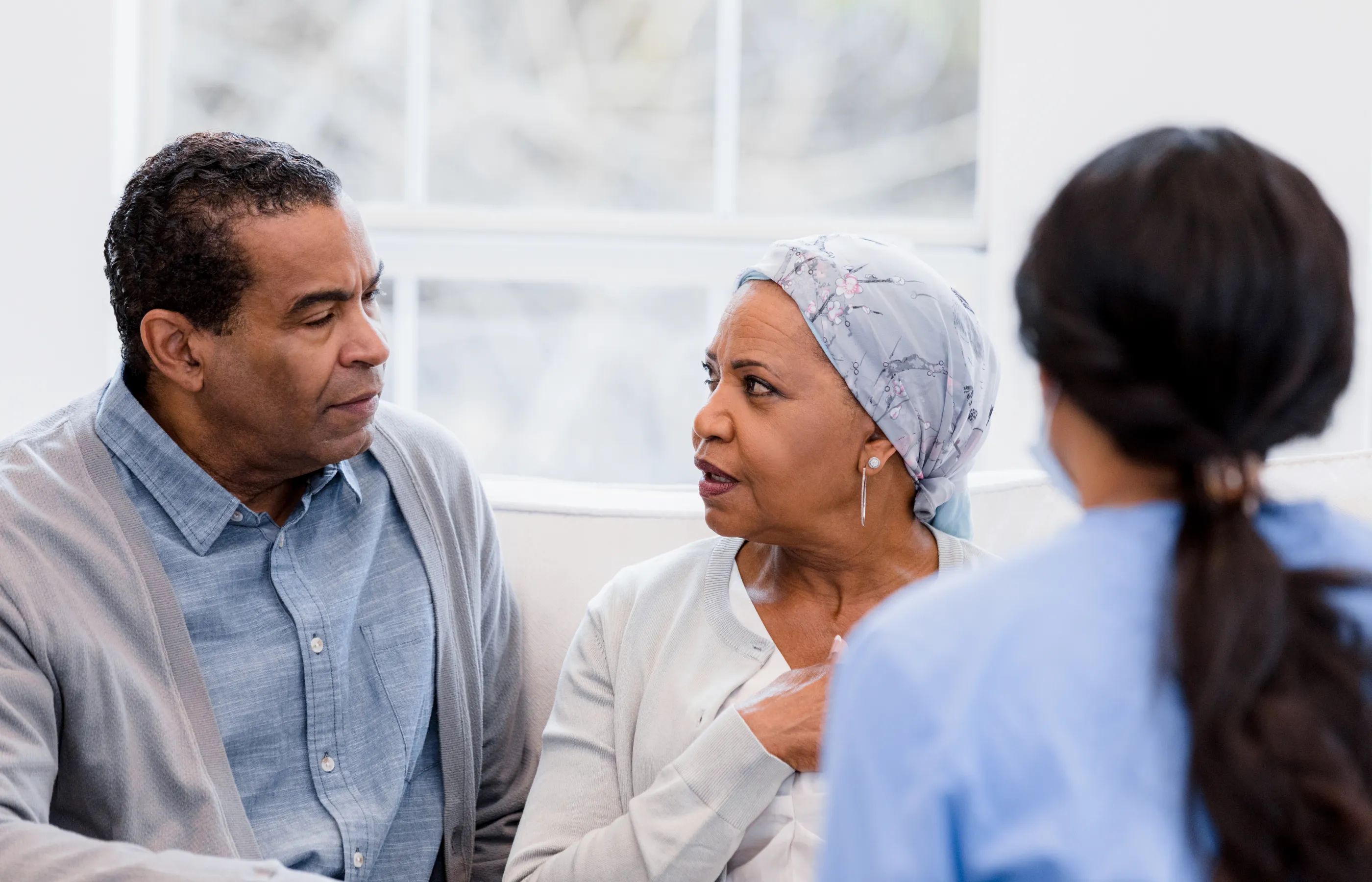 A mature couple is looking at each other and talking as they sit with a nurse. 