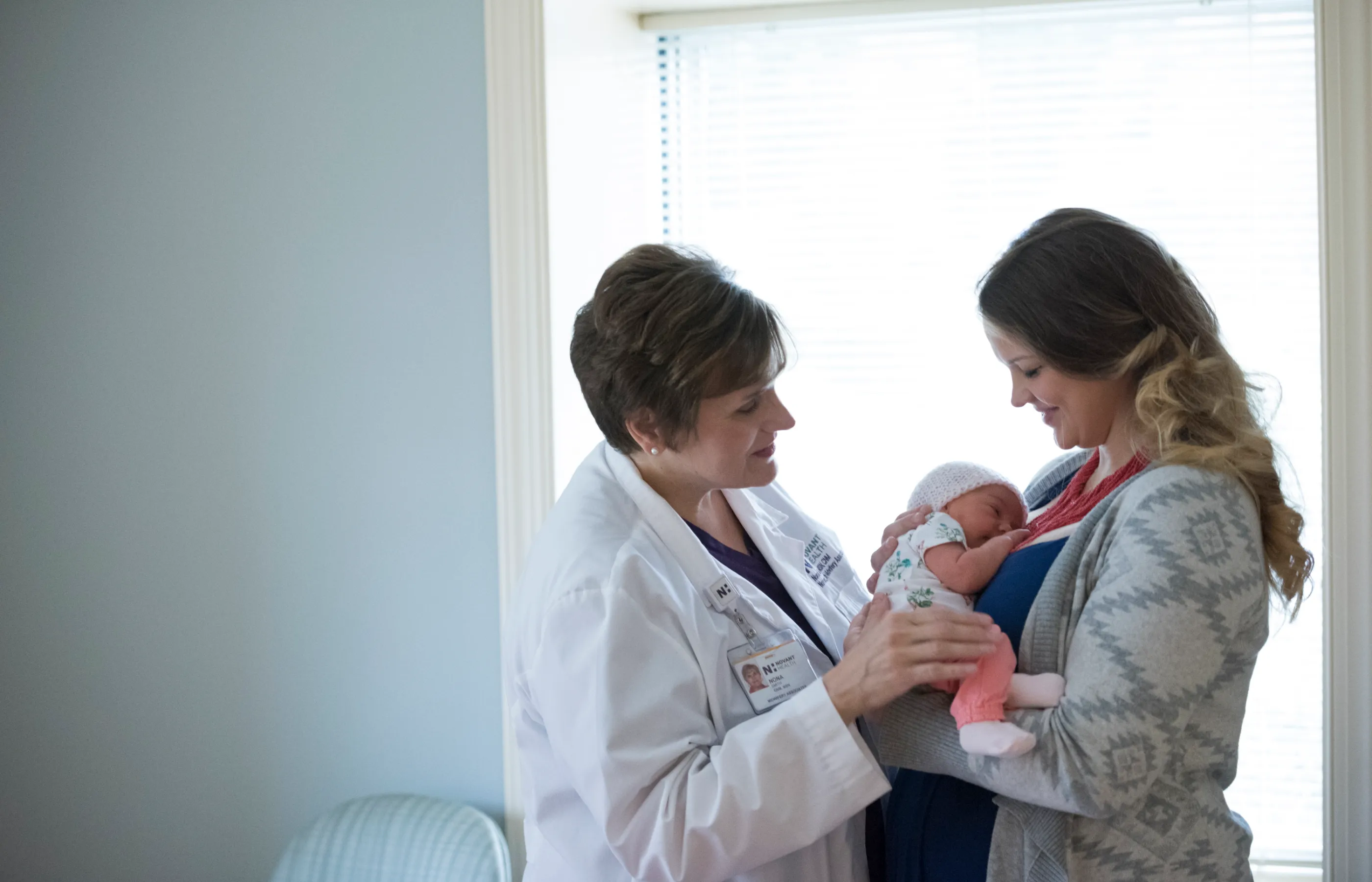 A Novant Health midwife is standing across from a mother as she holds her newborn. 